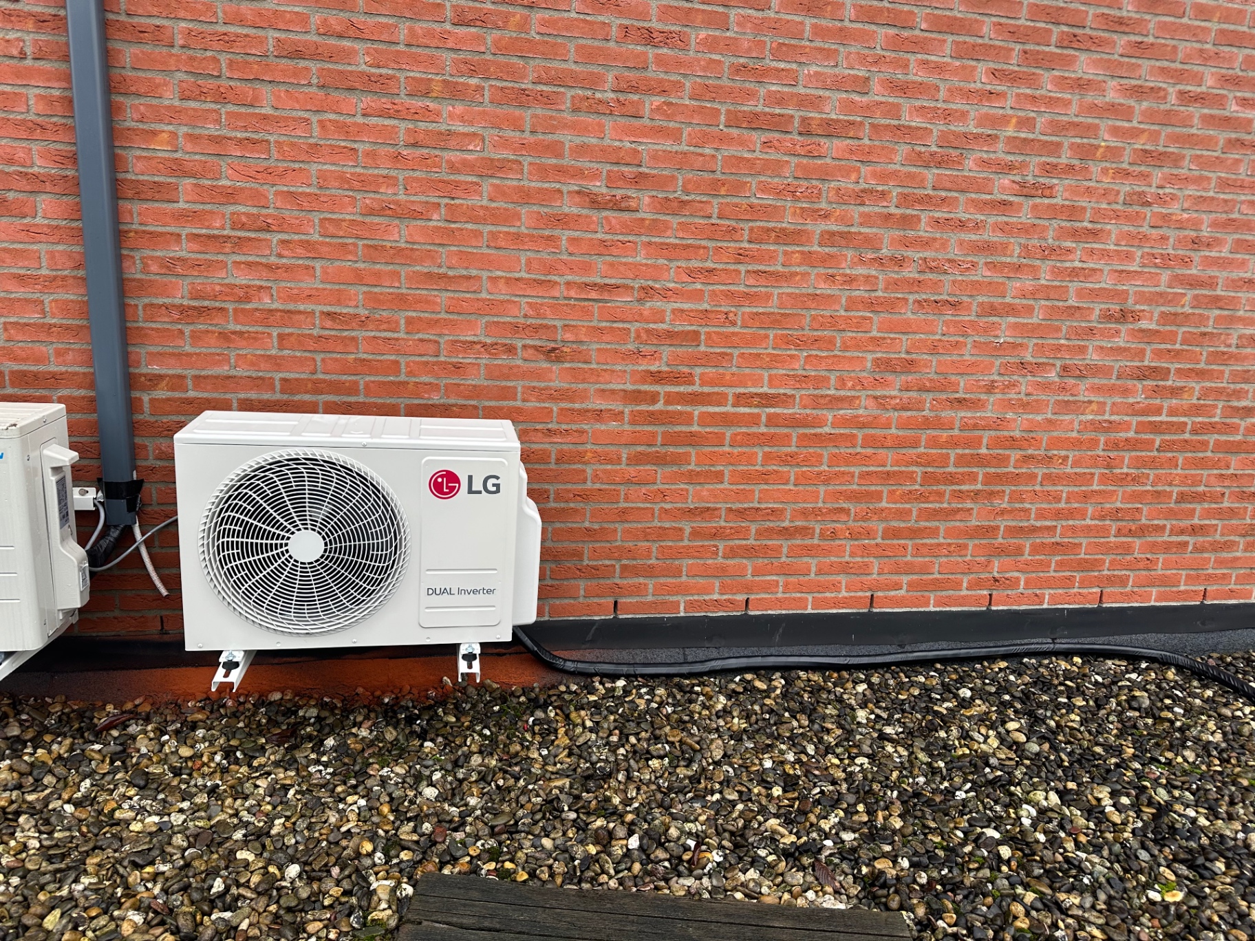 LG DUAL Inverter buitenunit op trillingsdempende voeten naast een bakstenen gevel