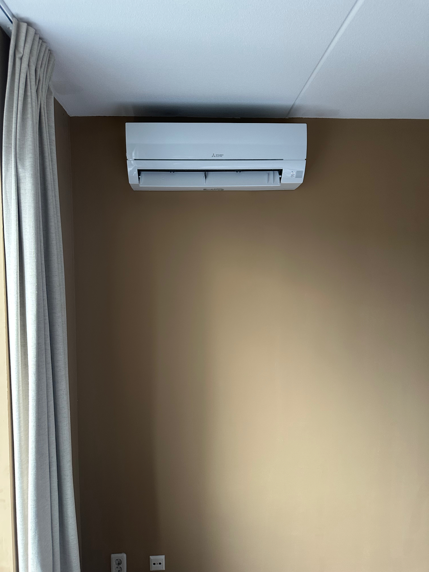 Mitsubishi Electric binnenunit strak onder het plafond aan een bruine wand
