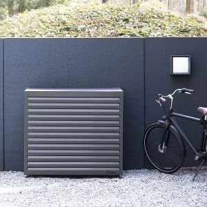 Grijze airco-omkasting tegen een donkere tuinschutting