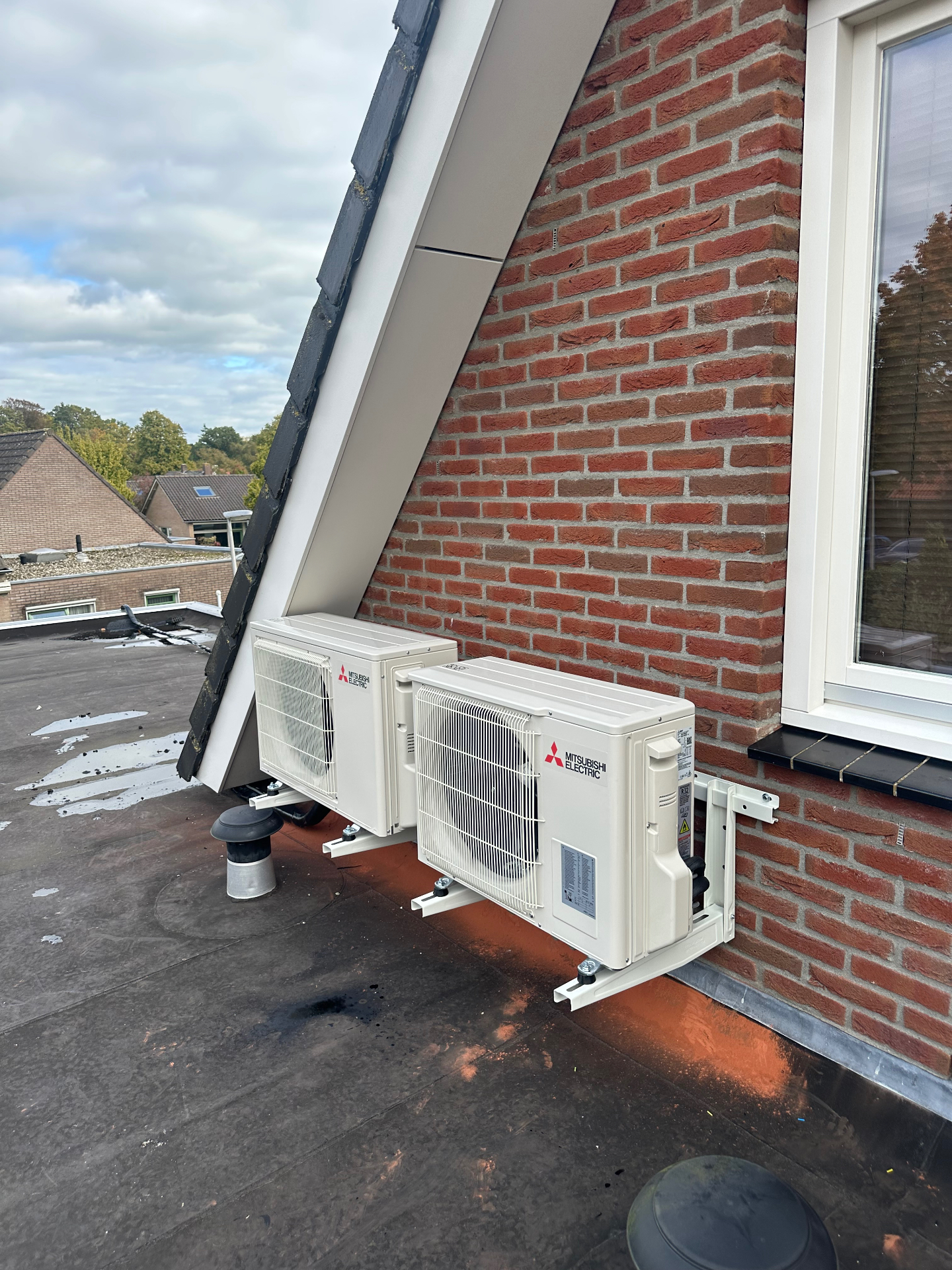 Twee Mitsubishi Electric buitenunits op een plat dak tegen een bakstenen gevel